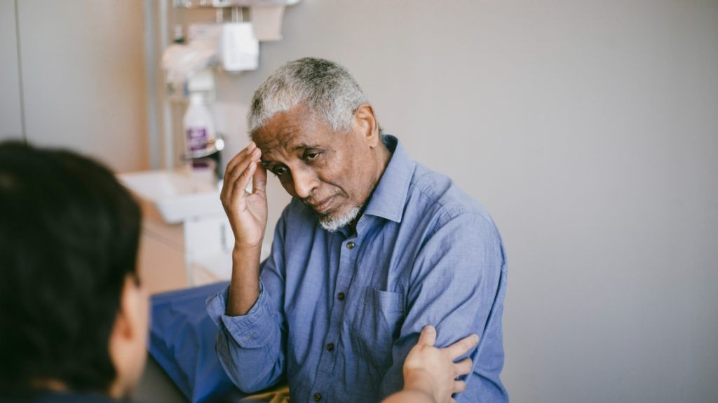An older adult male gets consoled by a medical professional in a doctor's office about his cholesterol test results