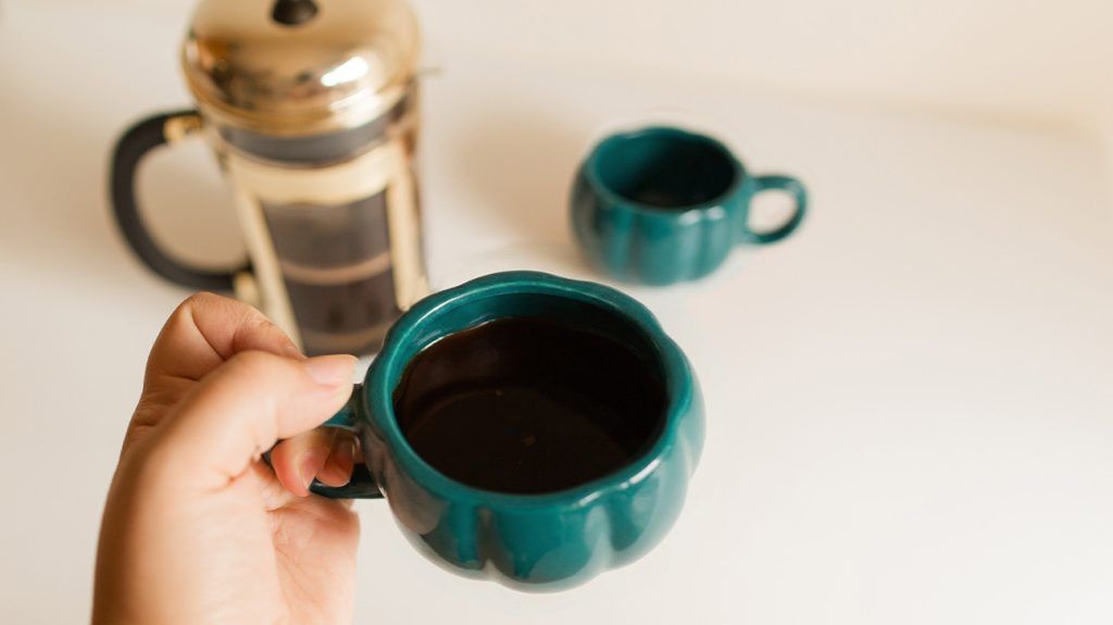 A person holding a cup of black coffee with another cup in the background