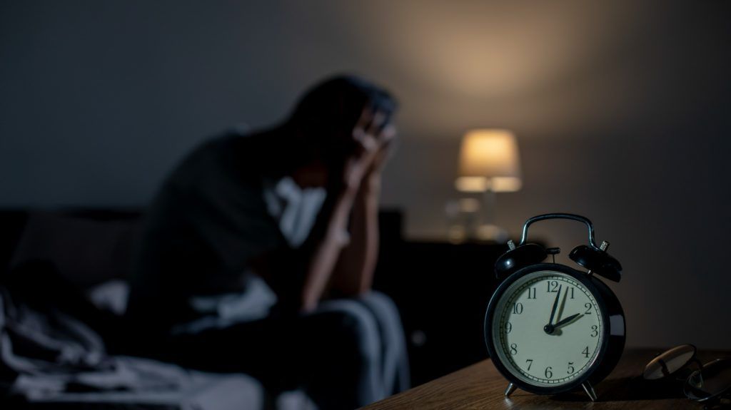 An older adult sitting in bed because they cannot sleep due to insomnia.