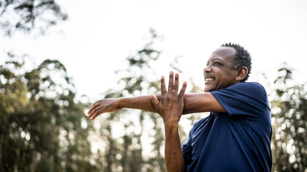 An older adult male stretching in a park outside