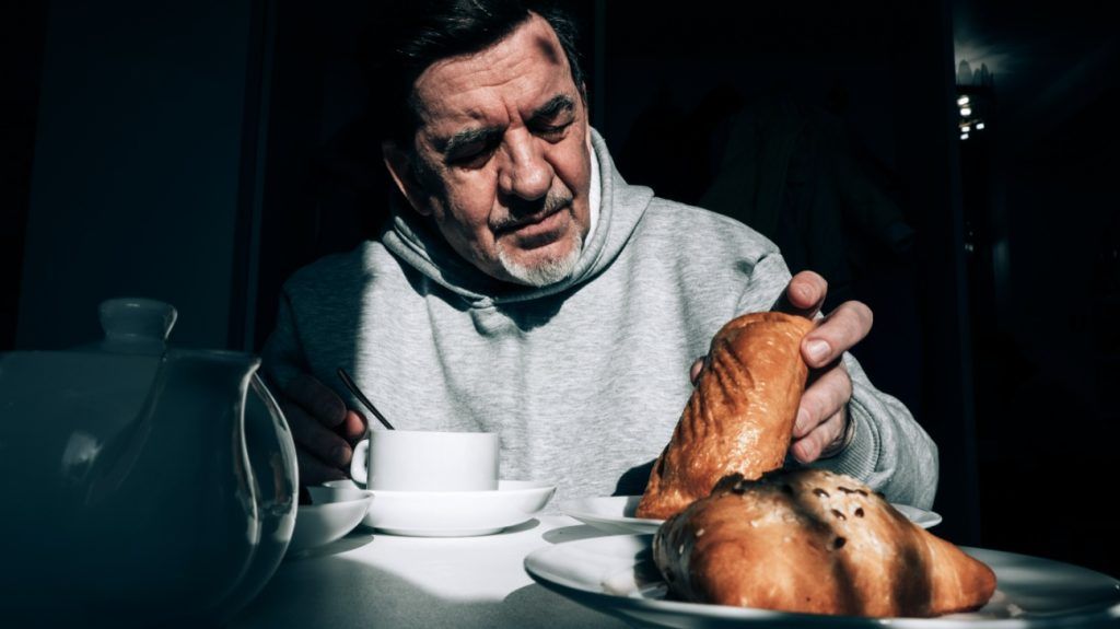 A man drinks tea and eats pastries at a table in bright sunlight