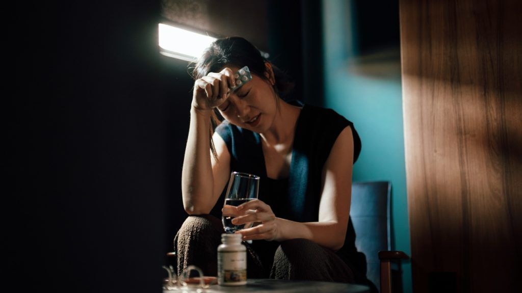 Asian woman pictured with her head leaning against her arm, holding a medication blister pack