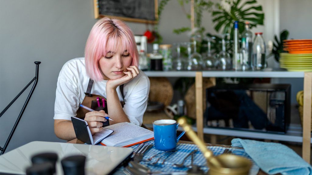 A 20s-something young woman who has schizophrenia is making notes on two notepads, contemplating