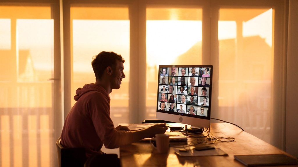 Man smiling through burnout on yet another Zoom meeting, needing to set work boundaries for himself