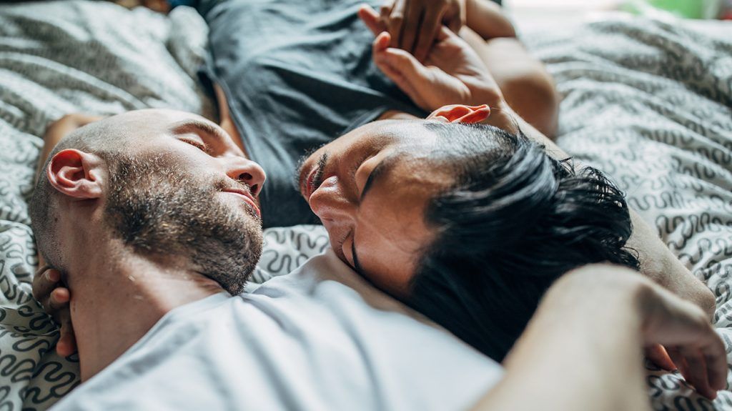 Male couple lying in bed looking at each other lovingly