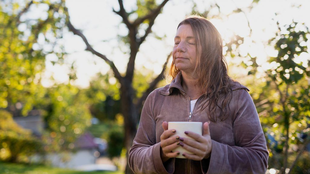 Woman with her eyes closed outdoors, cradling a cup in her hands