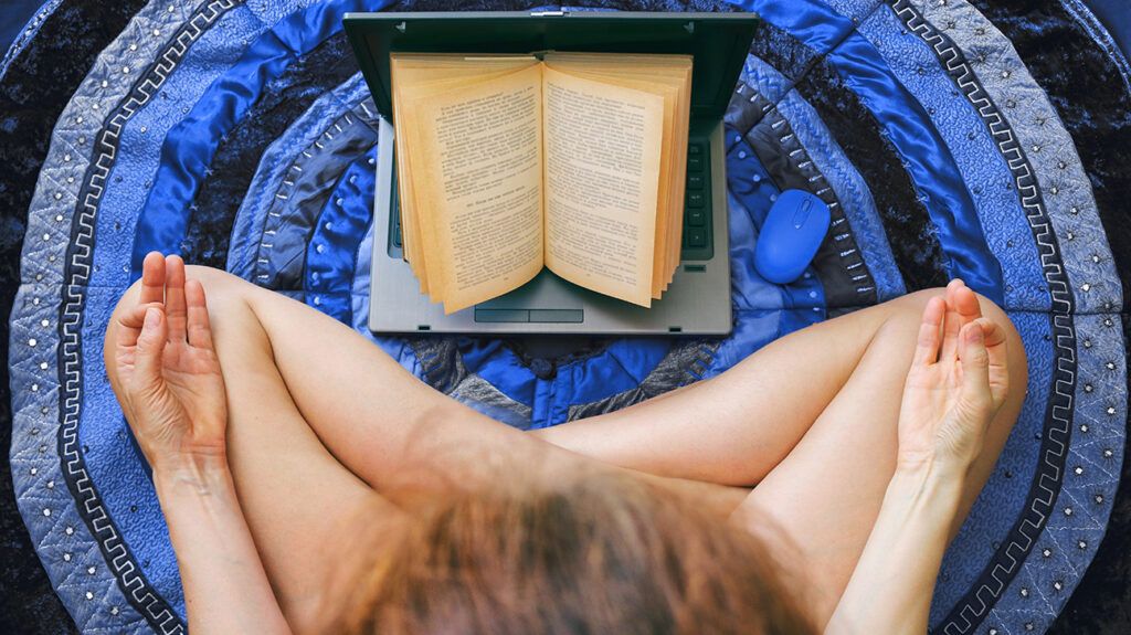 Person sitting cross-legged on a blue rug, meditating while reading a book