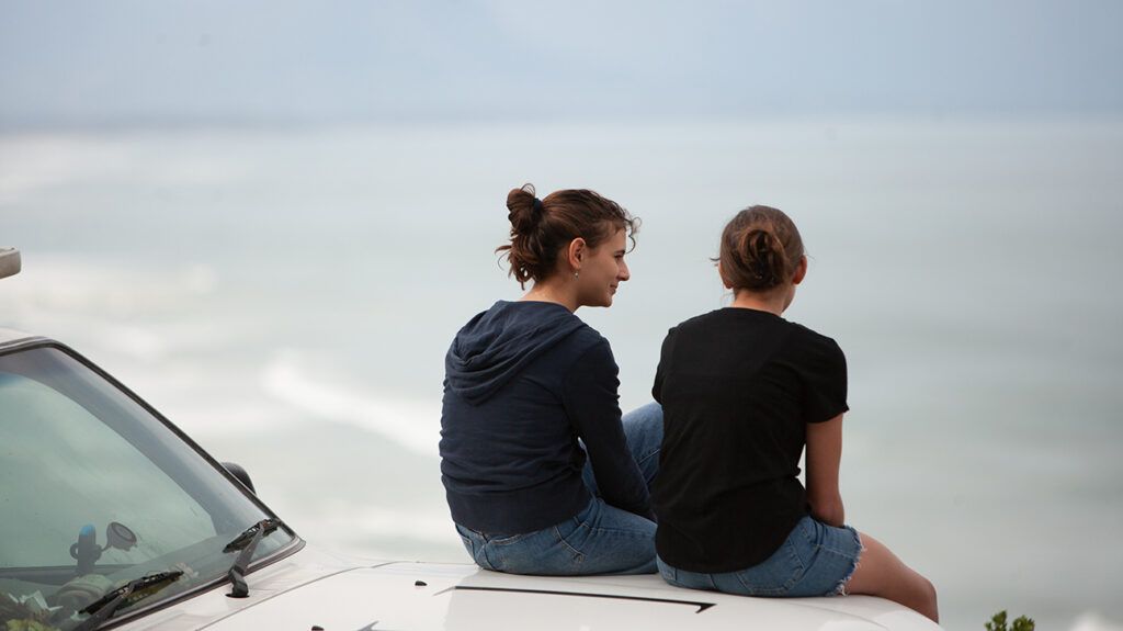 https://media.post.rvohealth.io/wp-content/uploads/sites/4/2021/07/two-girls-sitting-on-car-talking-ocean-1296x728-header-1024x575.jpg