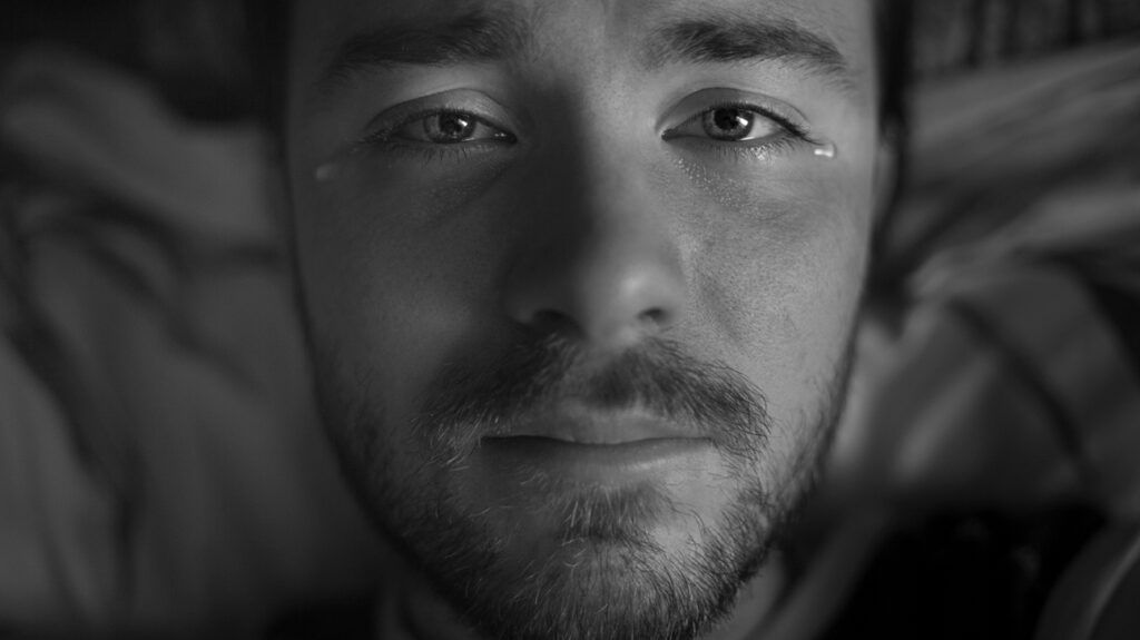 Man staring at the ceiling in bed, feeling more emotional than usual and wondering why