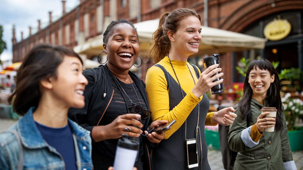 Group of female friends laughing and walking with coffees