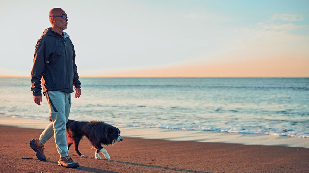 Older man walking dog on beach