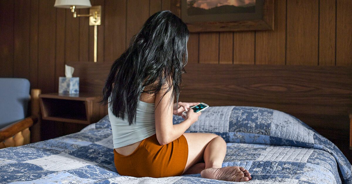 rear-view-woman-sitting-on-bed-hotel-roo