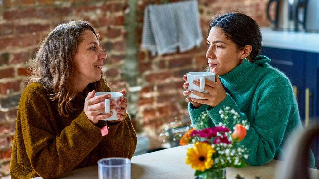 One friend offering supportive words to her sick friend, over tea