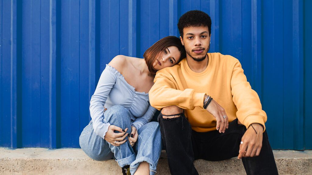 Young couple sitting against blue wall