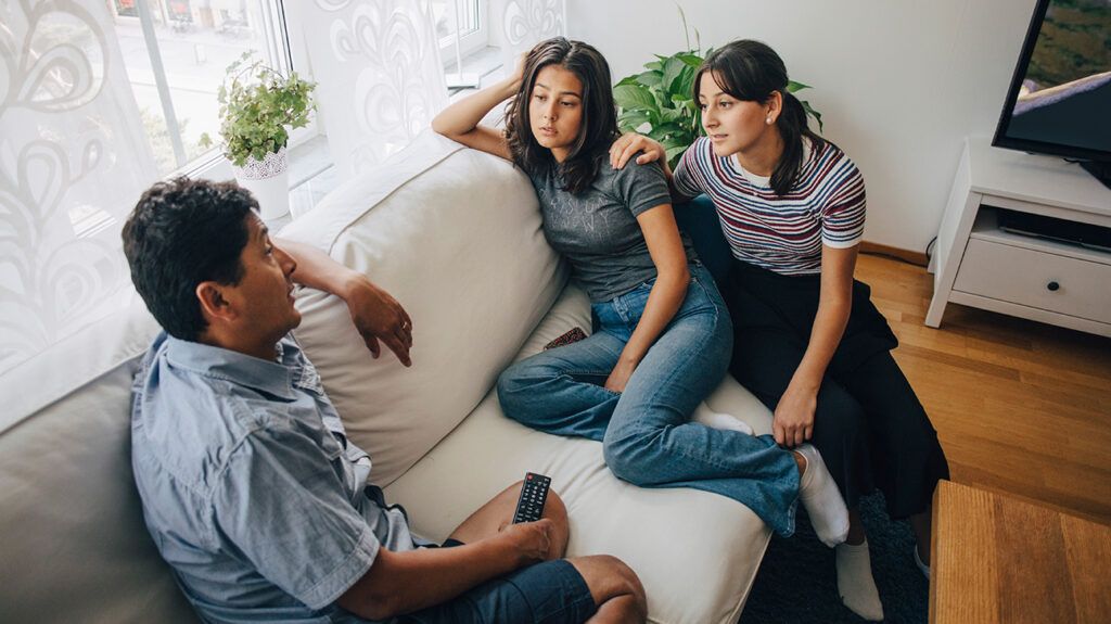 Dad talking to teen daughters on couch