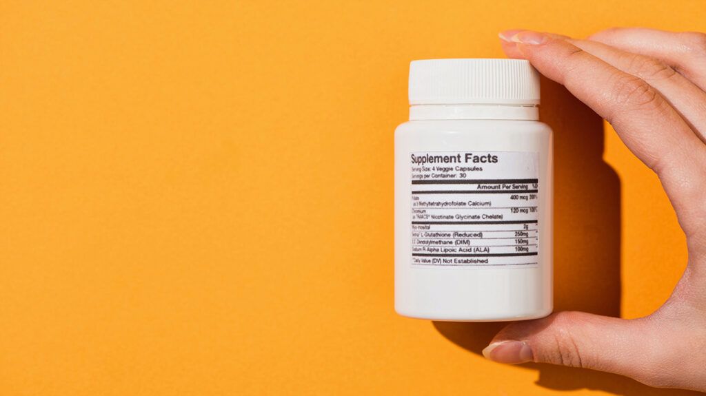 Hand holding a supplement container in front of an orange background