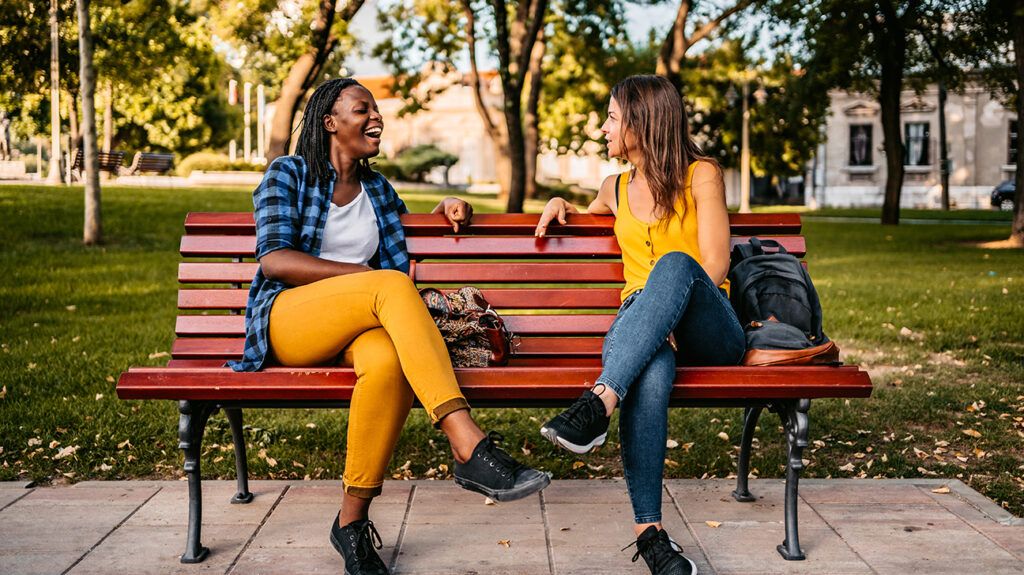 Two female friends talking on park bench