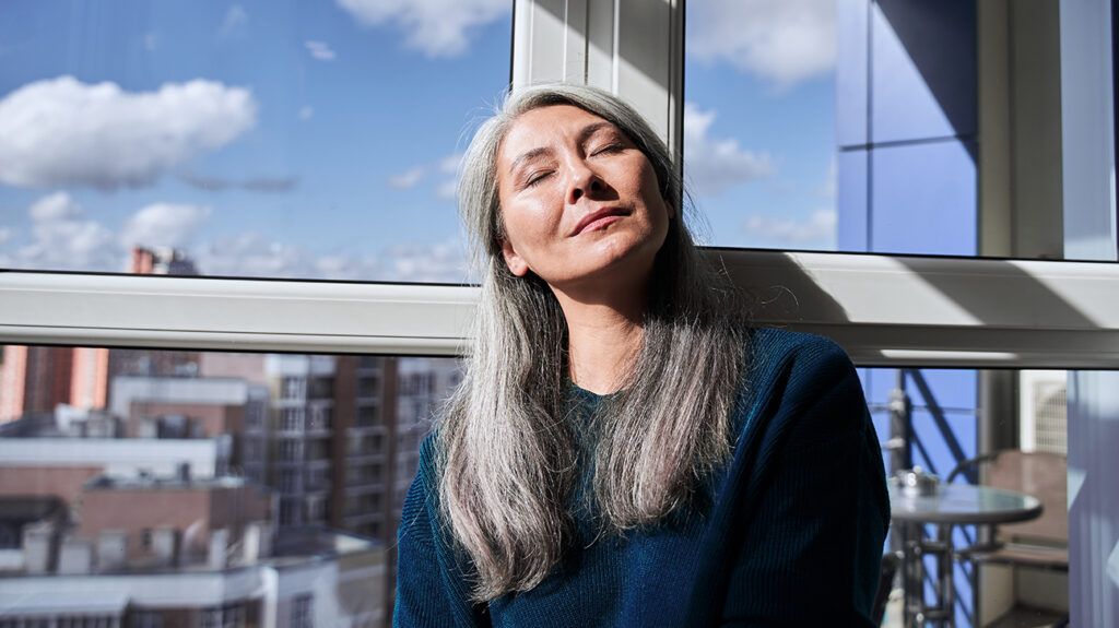 Woman sitting with her eyes closed, sun in her face, breathing mindfully