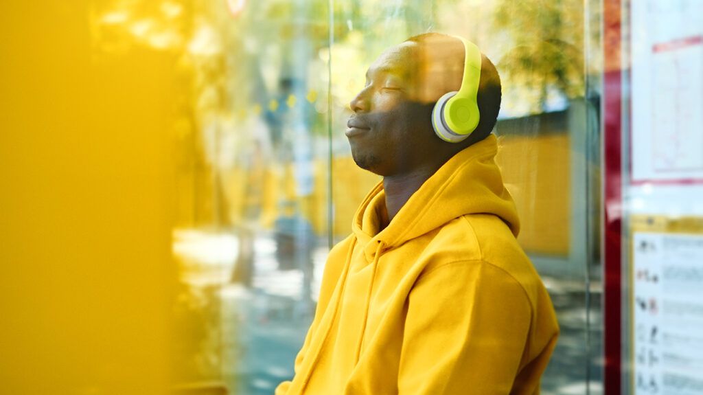 Man with headphones sitting at a bus stop with his eyes closed listening to an anxiety podcast