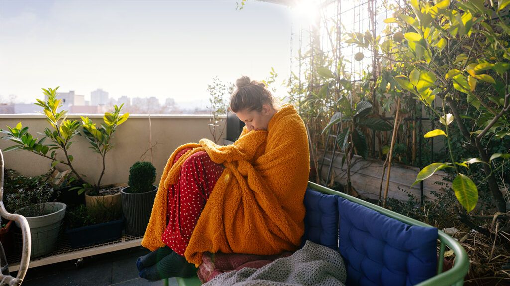 Woman wrapped in a blanket sitting outside on a patio with her eyes closed