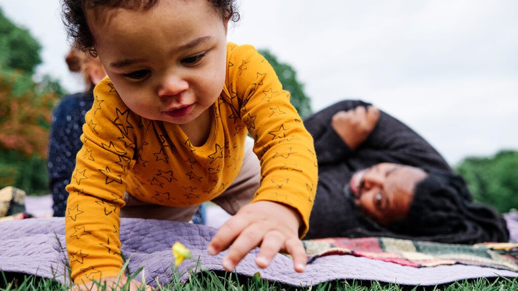 Baby crawling on a picnic blanket with parents watching