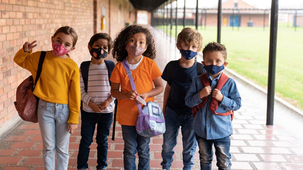 A group of children wearing masks in front of school