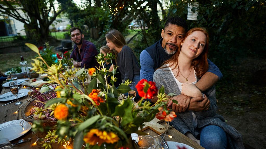 Mature man embracing younger woman at garden dinner party