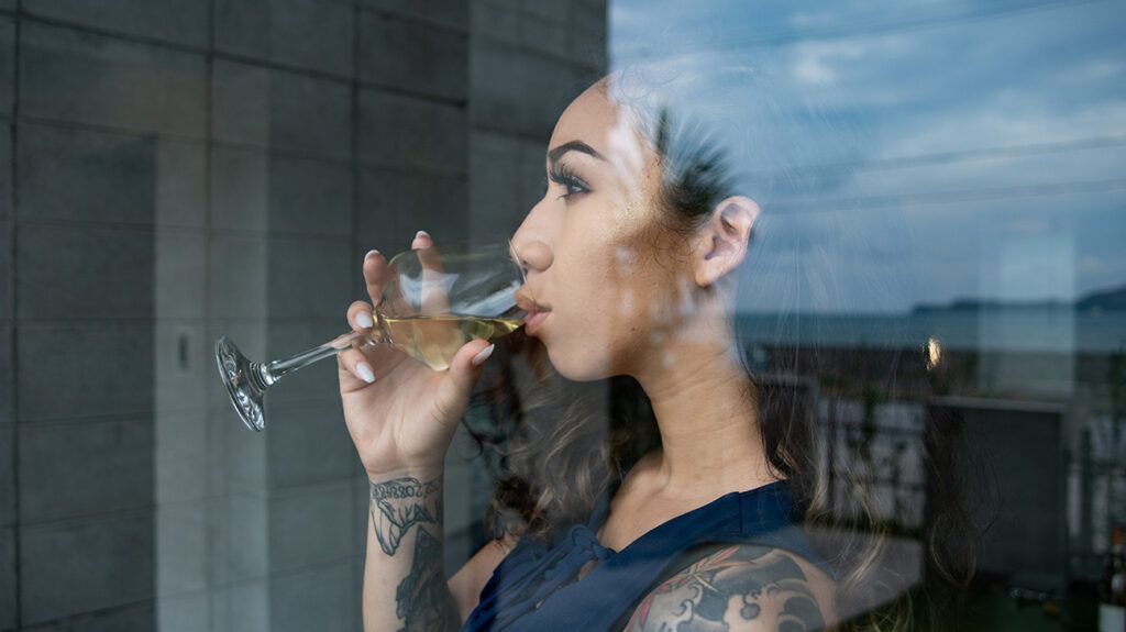 A person drinking a glass of wine while looking mindfully out the window