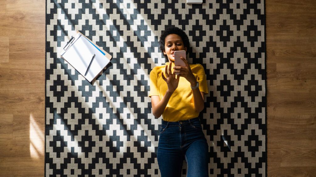 Woman lying on a carpet looking at mental health apps on her phone