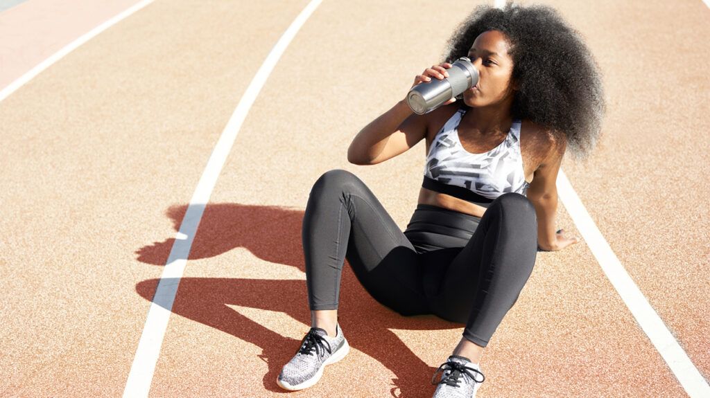 Woman runner sitting down on the track drinking from water bottle