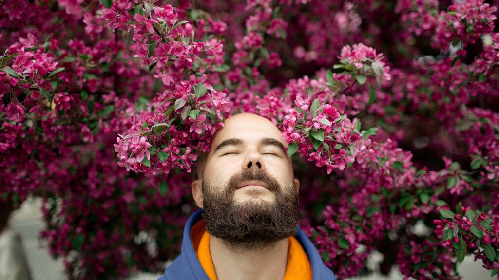 Bearded man with eyes shut under flower tree
