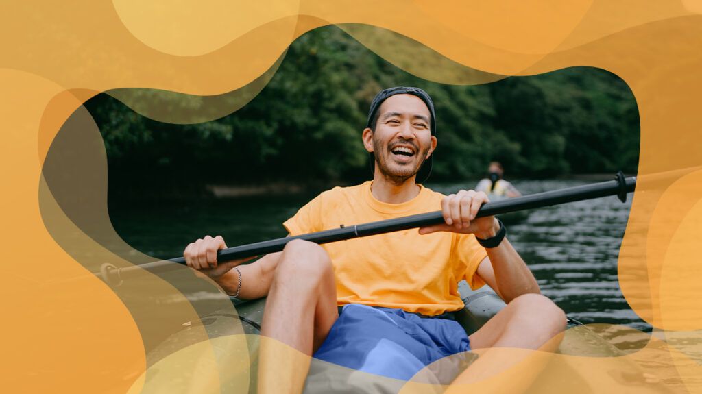 Man paddling a kayak in a river, laughing and smiling