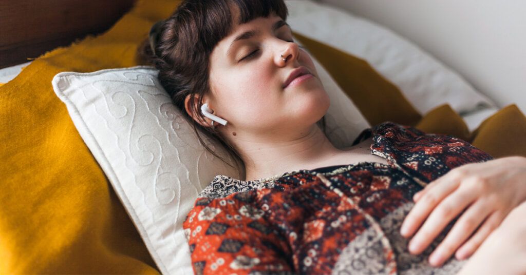 Young woman lying down with her eyes closed, meditating with headphones on