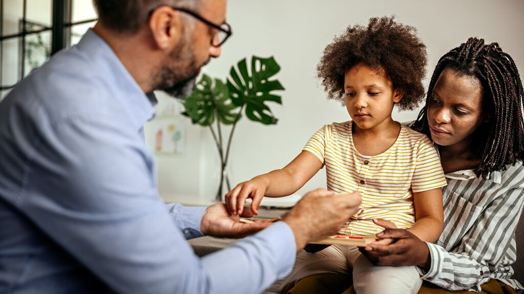 Mother and daughter in a therapy session with a male psychologist doing play therapy