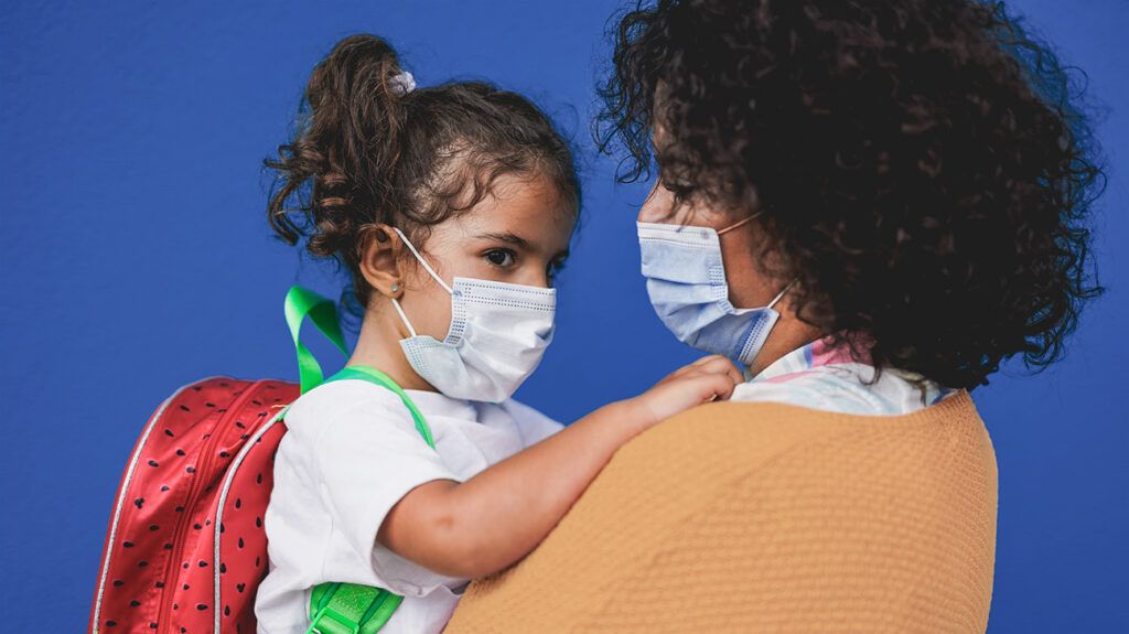 Mother holding young daughter with face masks on, talking about coronavirus