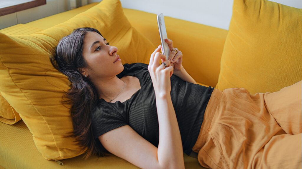 Young woman lying on couch looking at phone