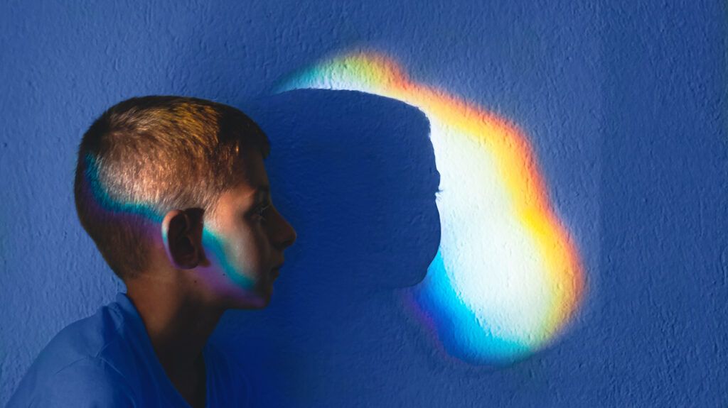 profile and silhouette of boy against wall with rainbow of sunlight