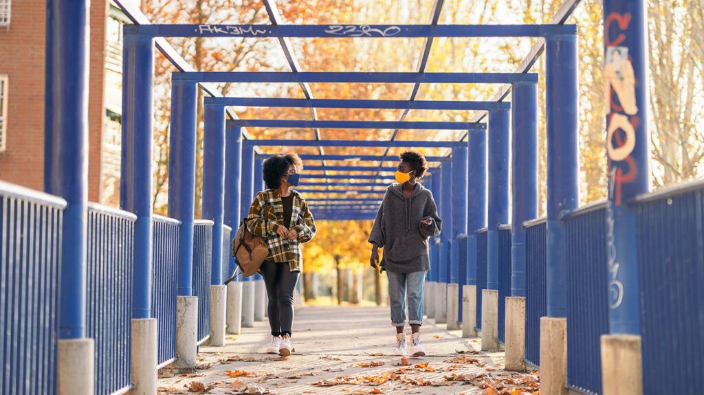 Two friends walking on bridge with face masks