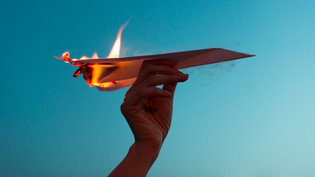 fragile paper airplane held in the air burning, like anxiety lit by anger