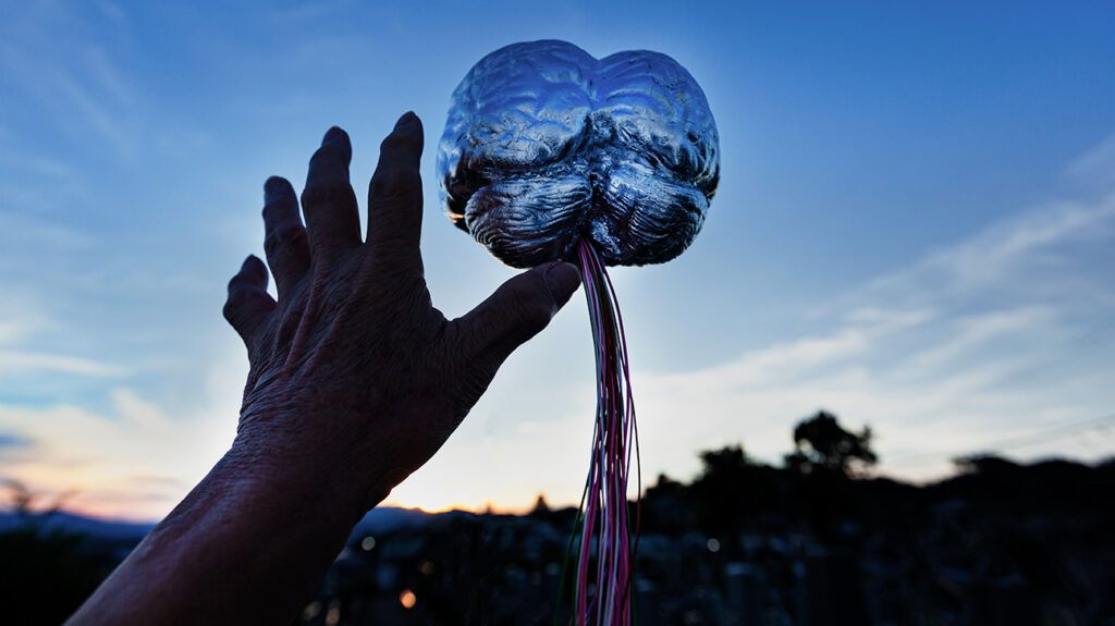 Hand reaching out to silver brain statue against blue sky