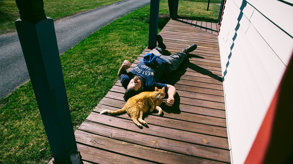 Man with covid fatigue syndrome lying down with his cat on his porch in the sun