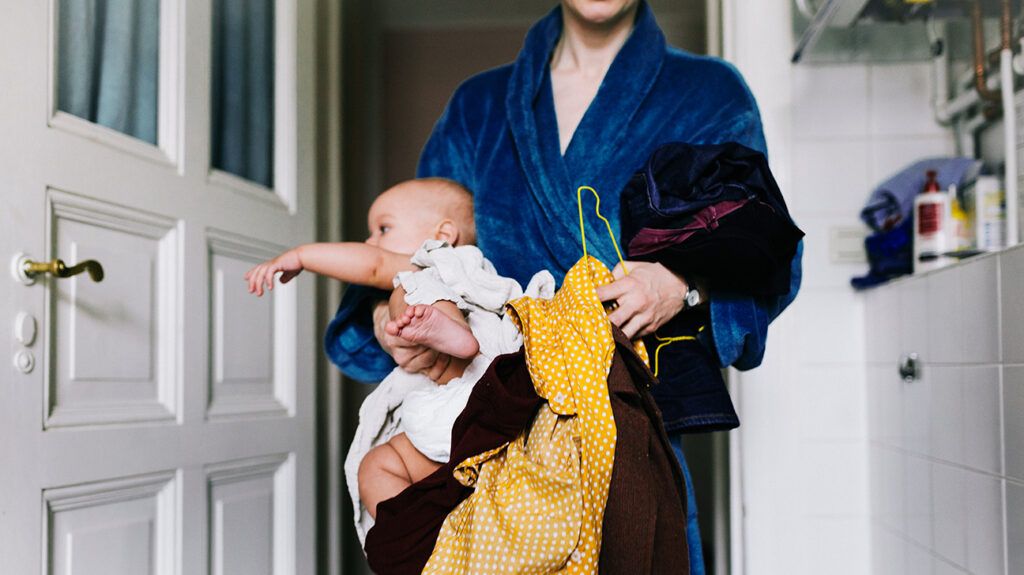 Working mother in bathrobe holding baby and work clothing
