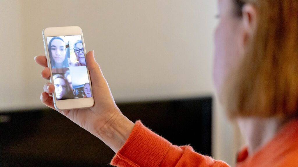 Older woman holding a phone making a video call to members of an online support group