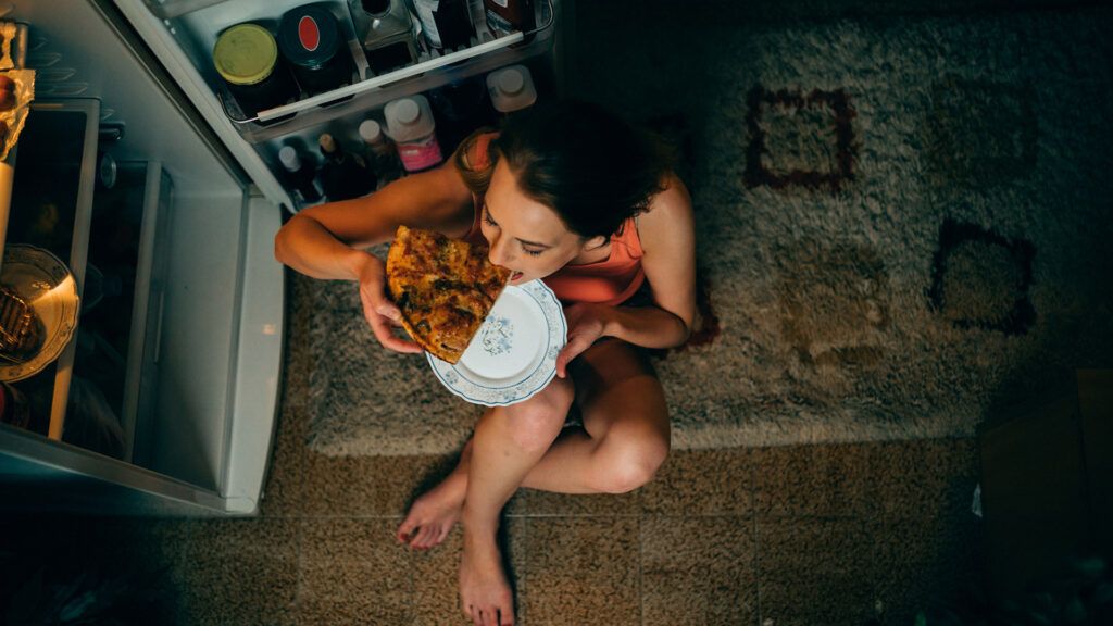 Woman eating pizza out of the fridge while asleep