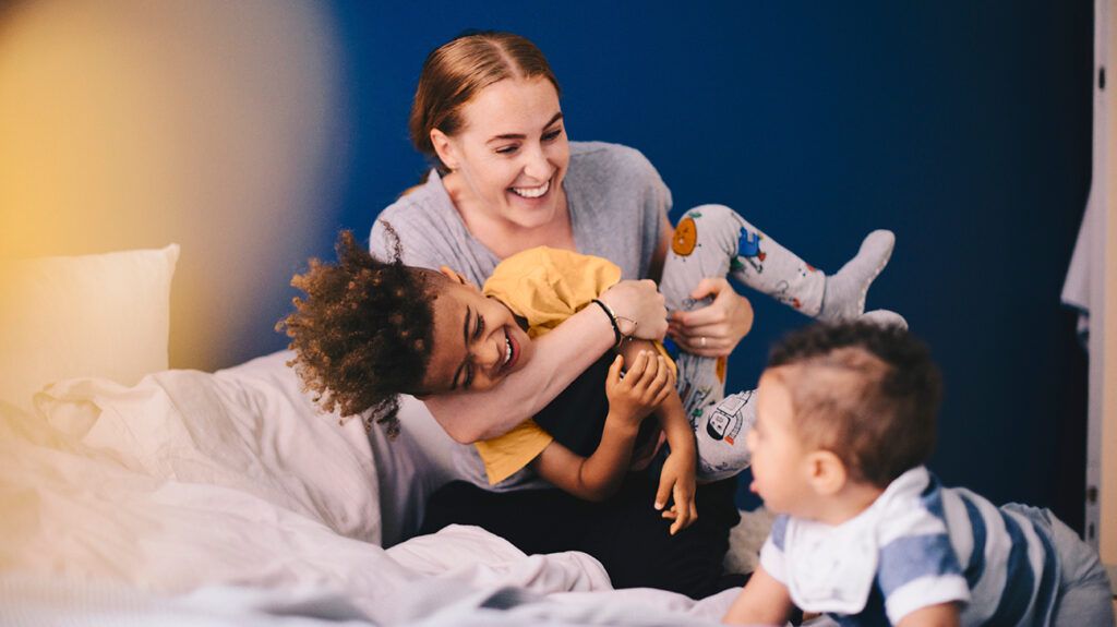 A smiling mother playing her two children on a bed