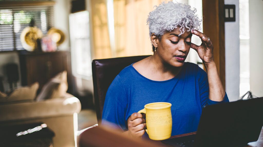 Woman with headache looking at computer with coffee