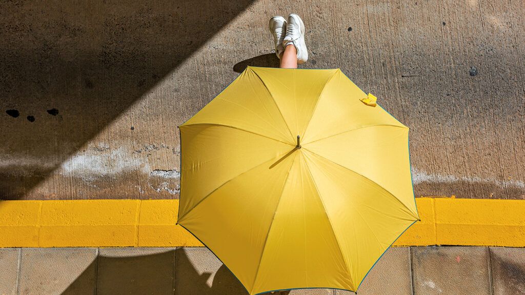 Person holding a yellow umbrella sitting on a street curb, viewed from above