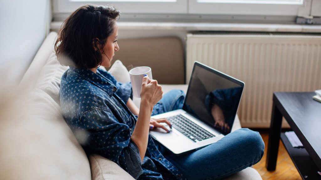 Woman sitting on a couch with a cup of coffee, taking an online anger management class on her laptop