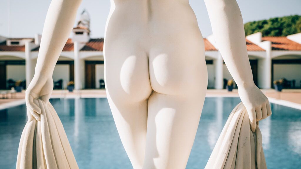 a nude statue standing in front of a swimming pool showing buttocks