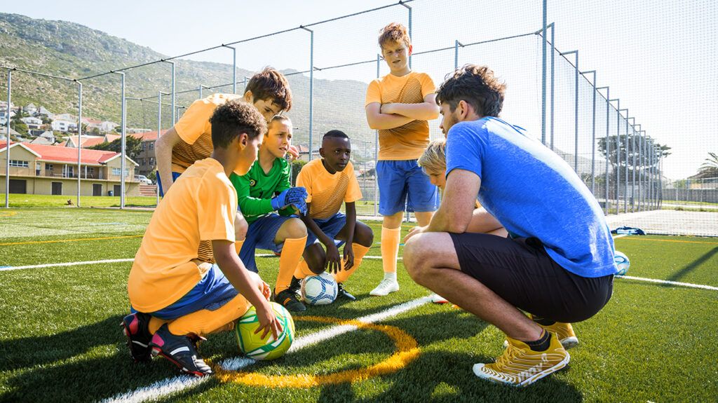 Soccer coach huddling with young players, using a strategy for one kid who has ADHD